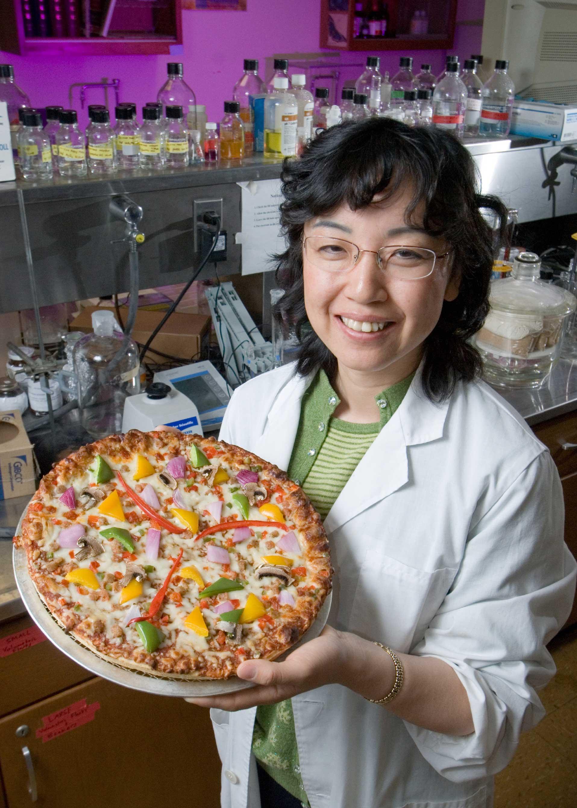 Woman smiling holding a pizza in a lab