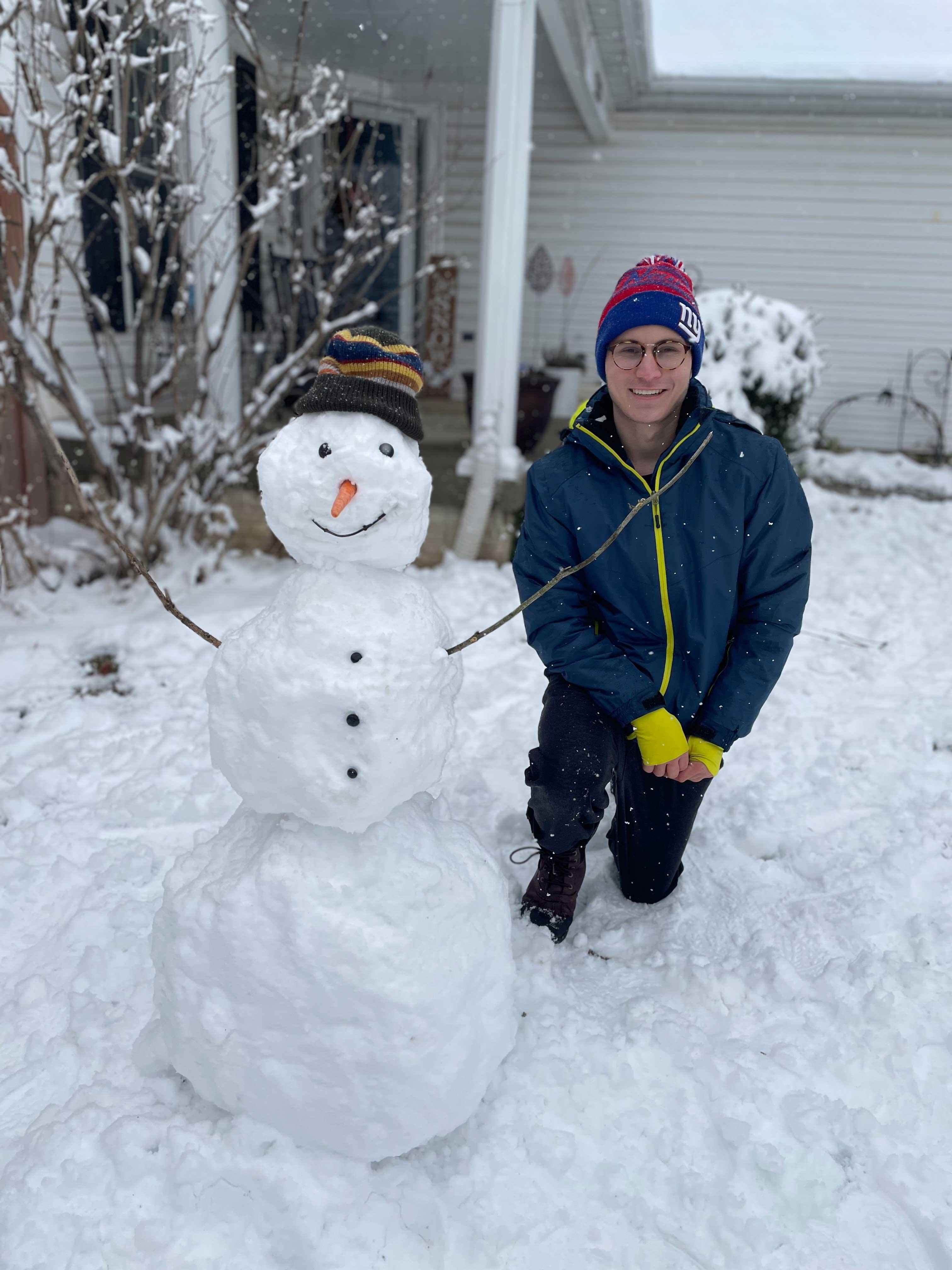 Joyful student kneeling with happy, hatted snowman.