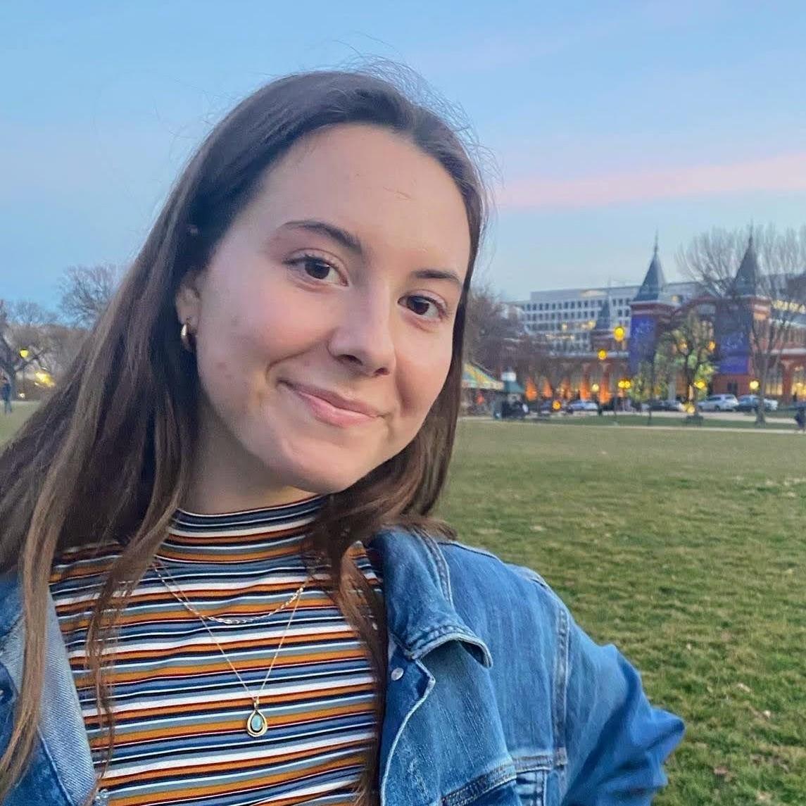 Olivia is standing on a grassy lawn, smiling at the camera