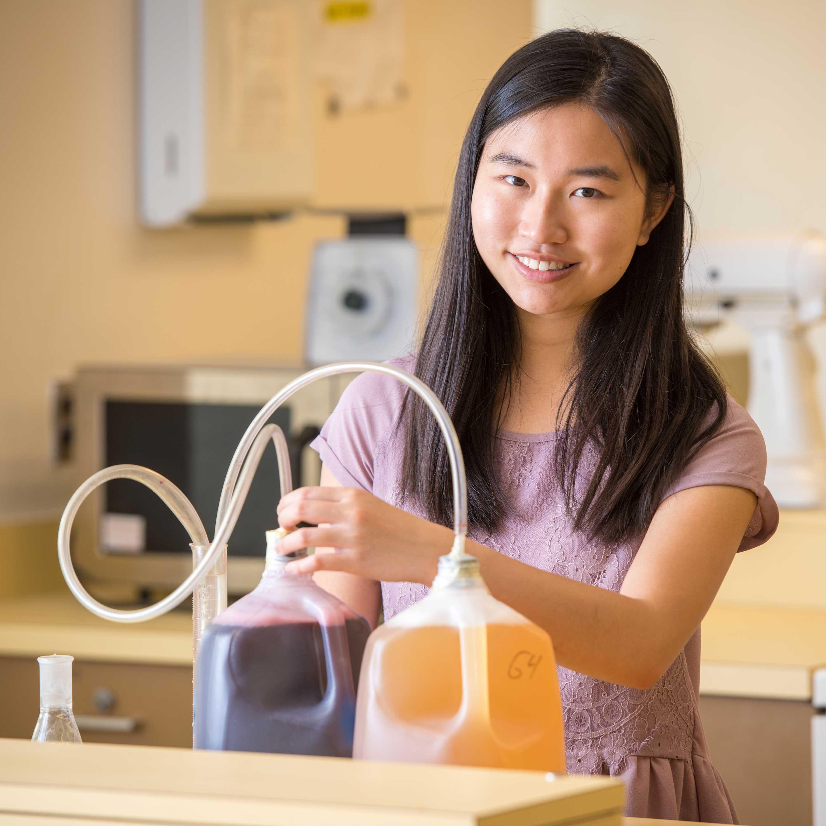 Student smiling while fermenting food with tubes going into two milk jugs