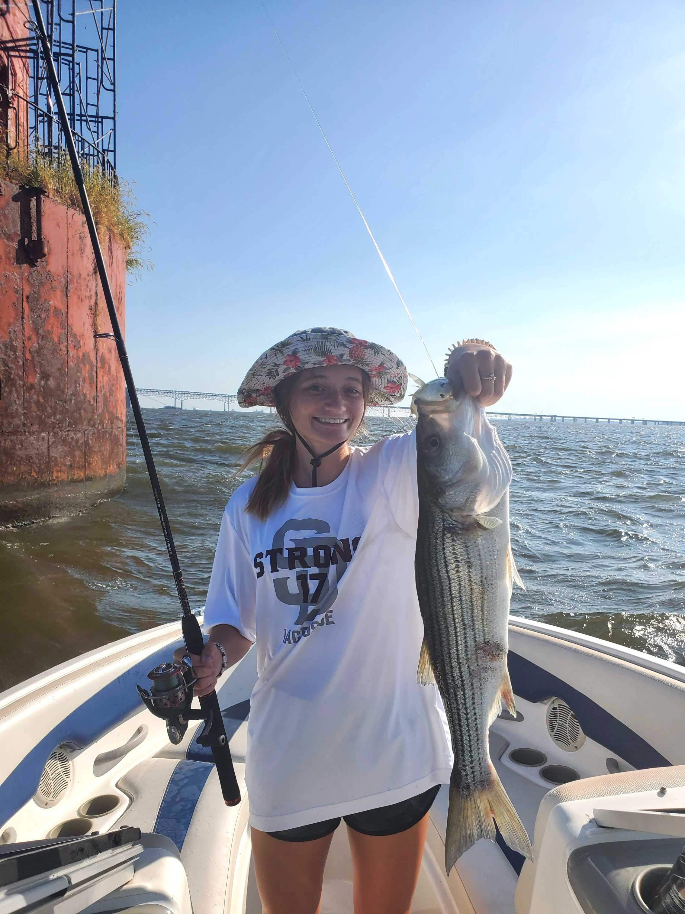 Happy hatted student presenting fresh fish catch on a boat.