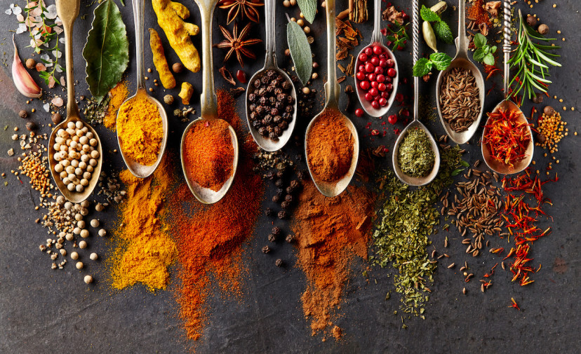 Whole spices and spoons full of ground spices laid out on a counter.