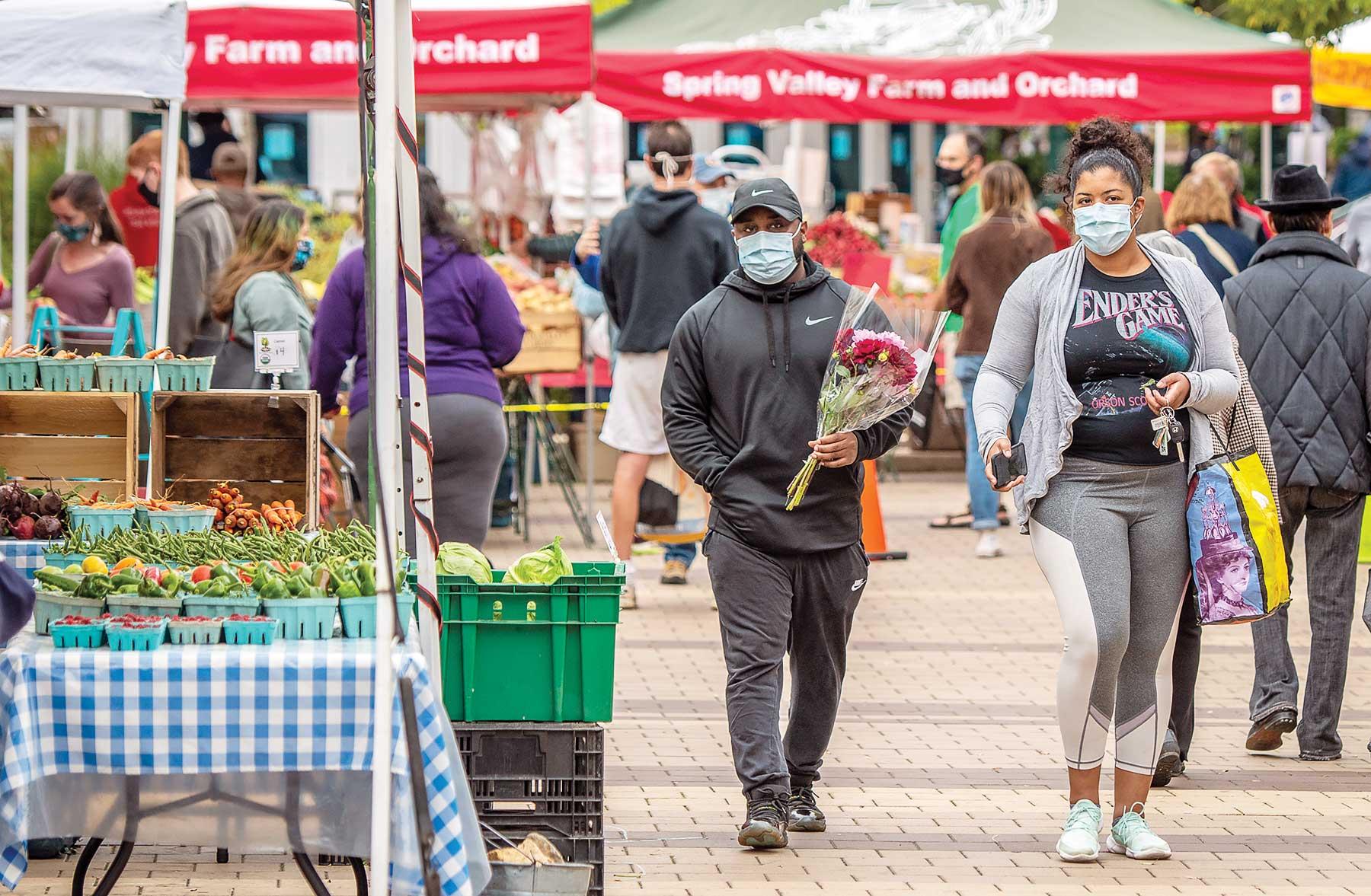 farmer’s market shoppers walking through produce stands. 