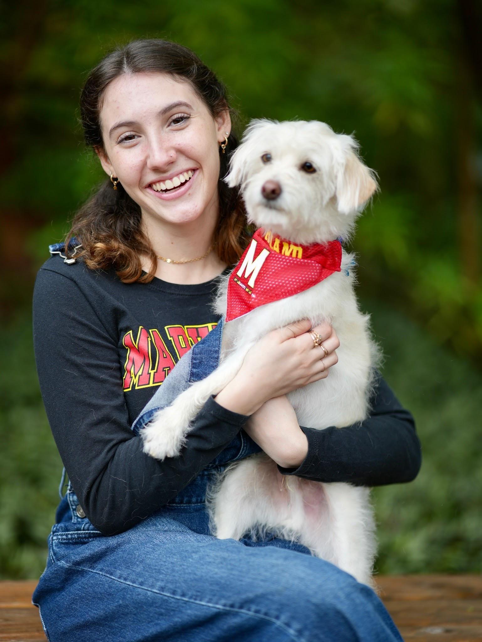 Naomi Rappaport. Smiling student in University of Maryland attire holding medium-sized white dog, also wearing University of Maryland wear!