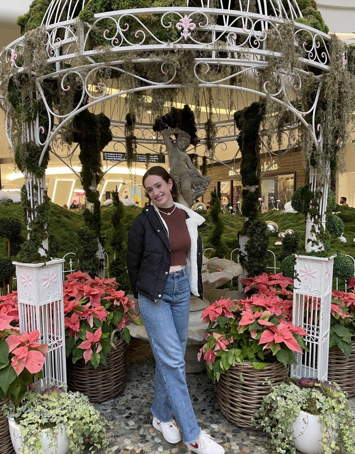 Natalie Cantagallo.  Smiling student in forefront of pink flowers and a lovely gardenscape.